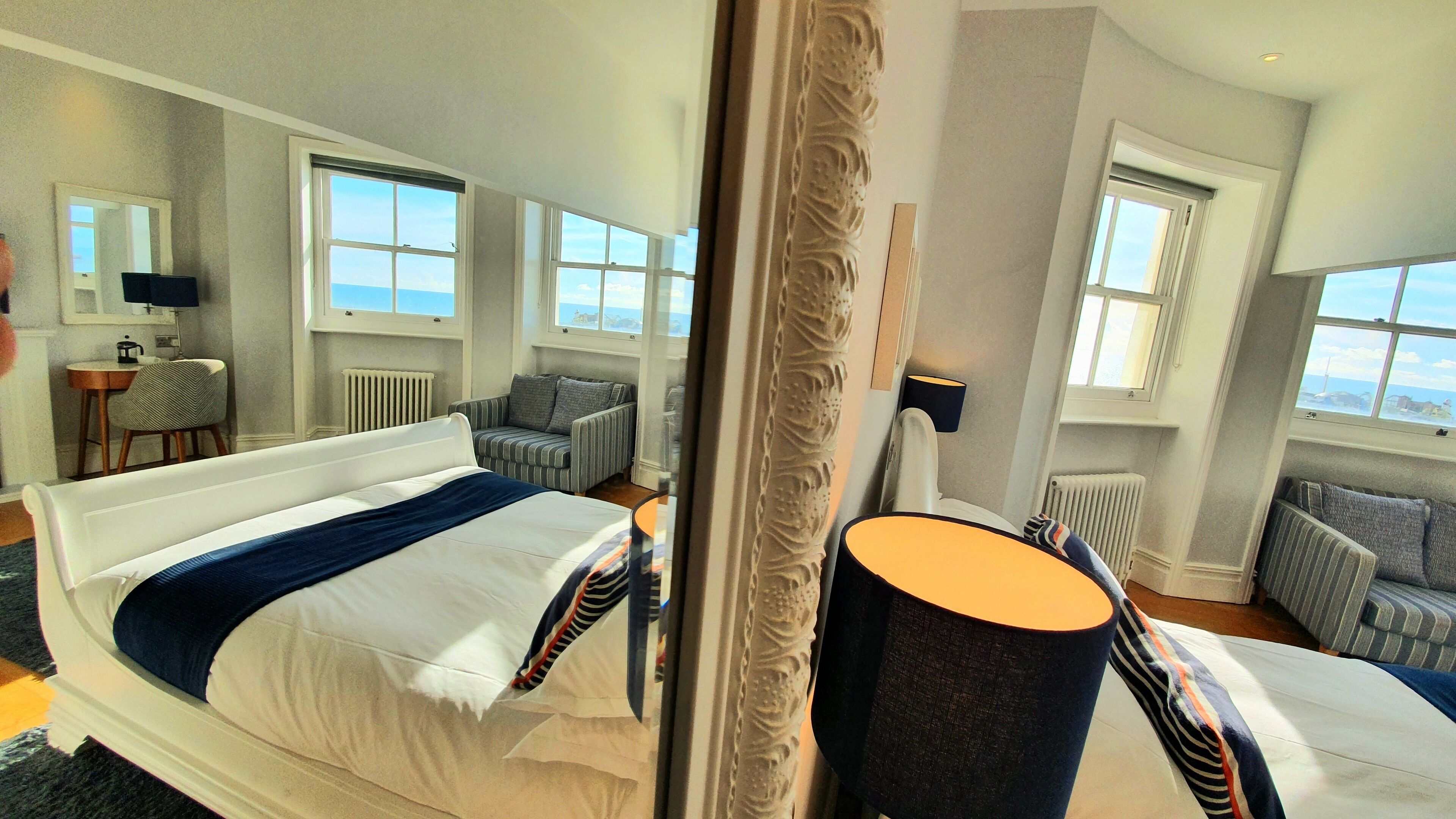 A hotel room with a large bed, a seating area with a chair and a sofa, a small table with a lamp, and large windows offering a view.