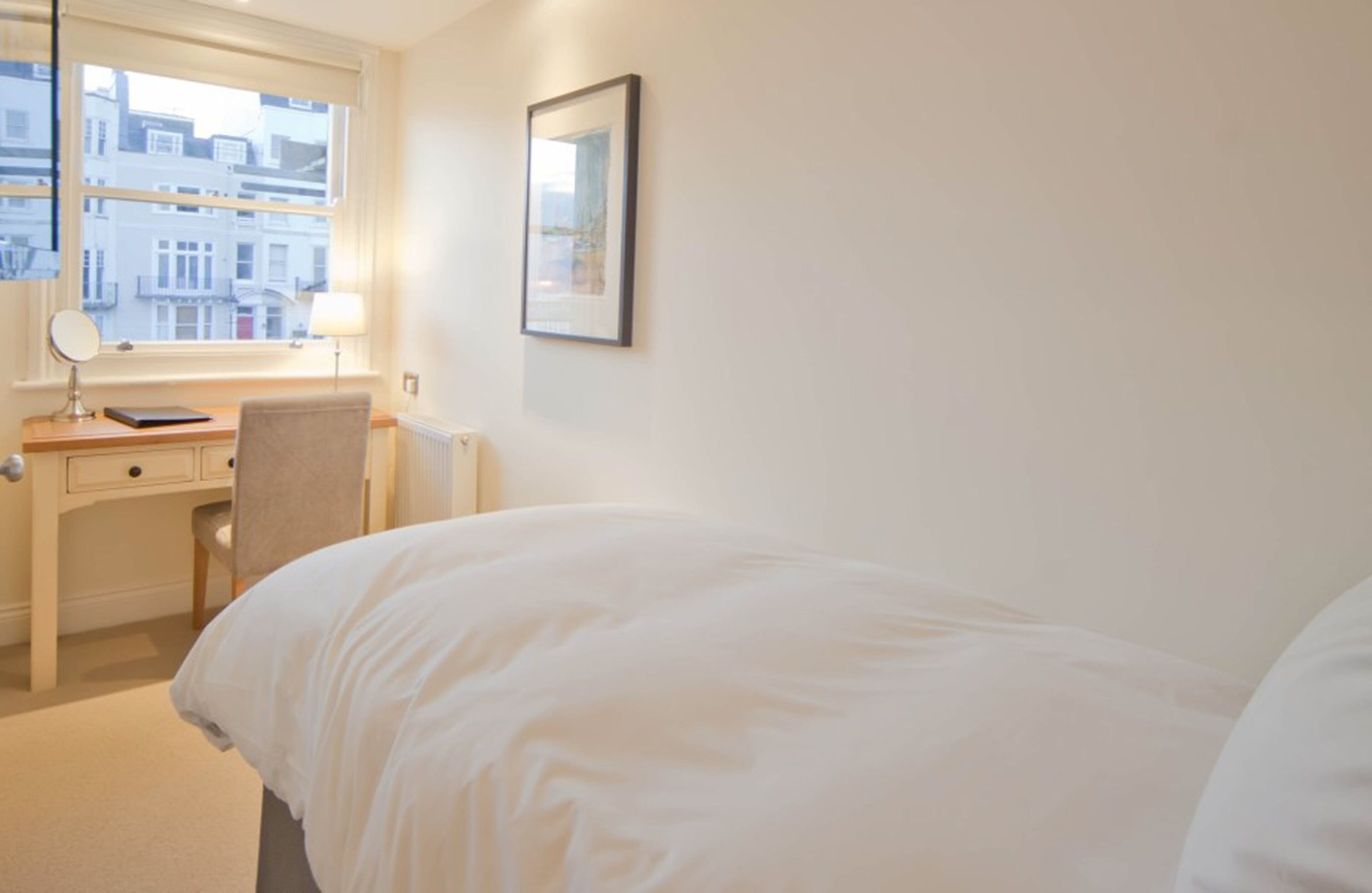 A hotel room with a bed, a desk with a chair, a lamp, and a window with a view of buildings.