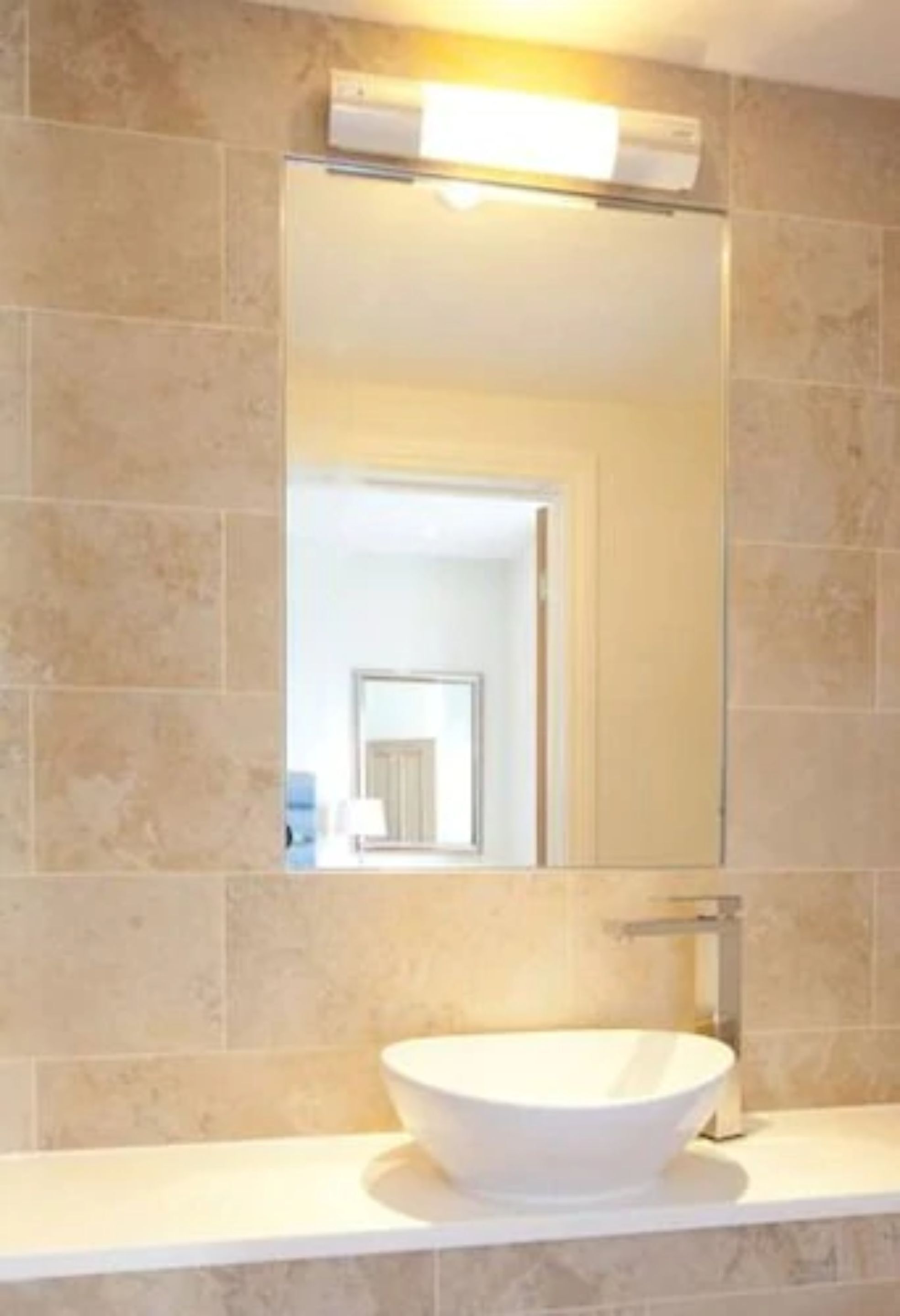 A bathroom with a white sink, a mirror, and beige tiles.