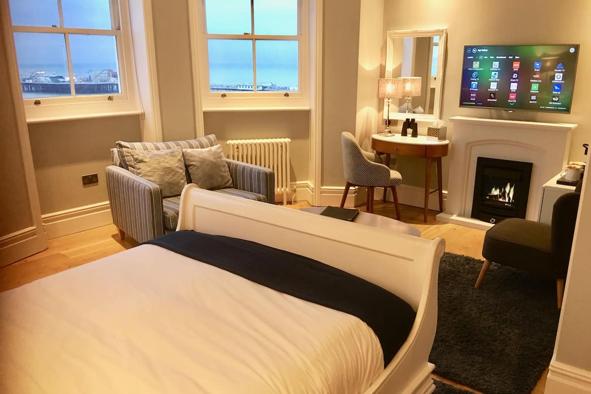 A bedroom with a bed, a desk, a chair, a fireplace, and a TV.
