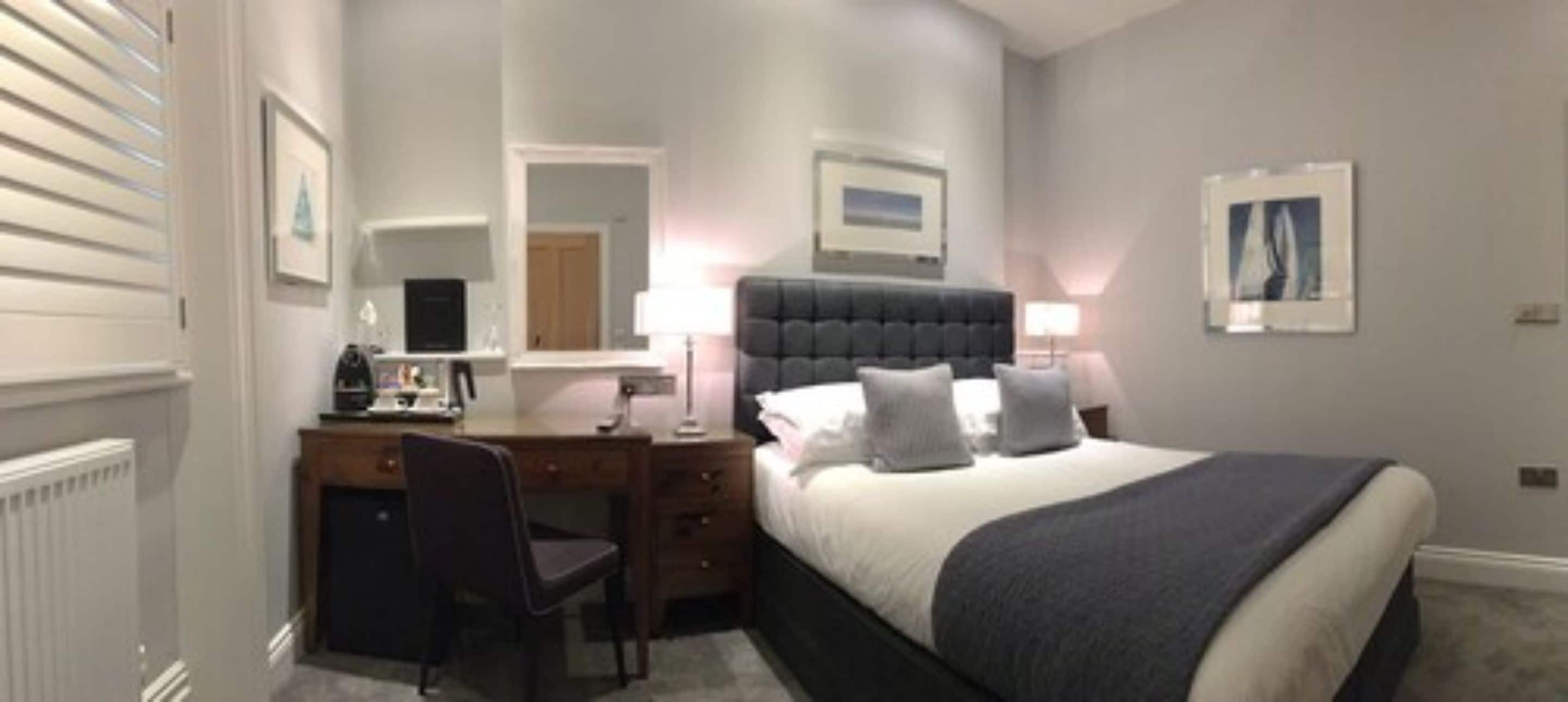 A hotel room with a bed, a desk, a chair, a lamp, and a mirror.