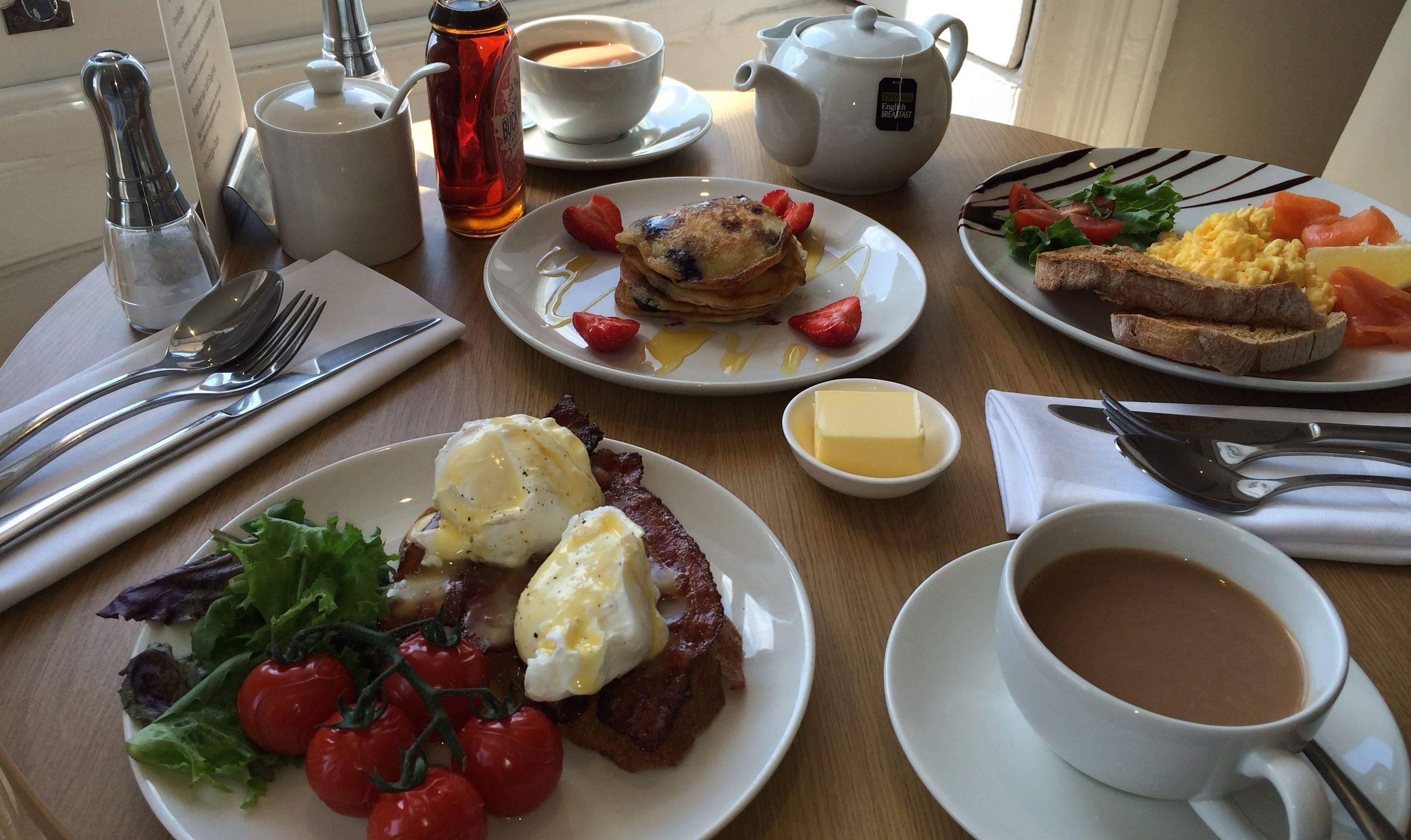 A breakfast table with various dishes including pancakes, scrambled eggs, toast, and a cup of coffee.
