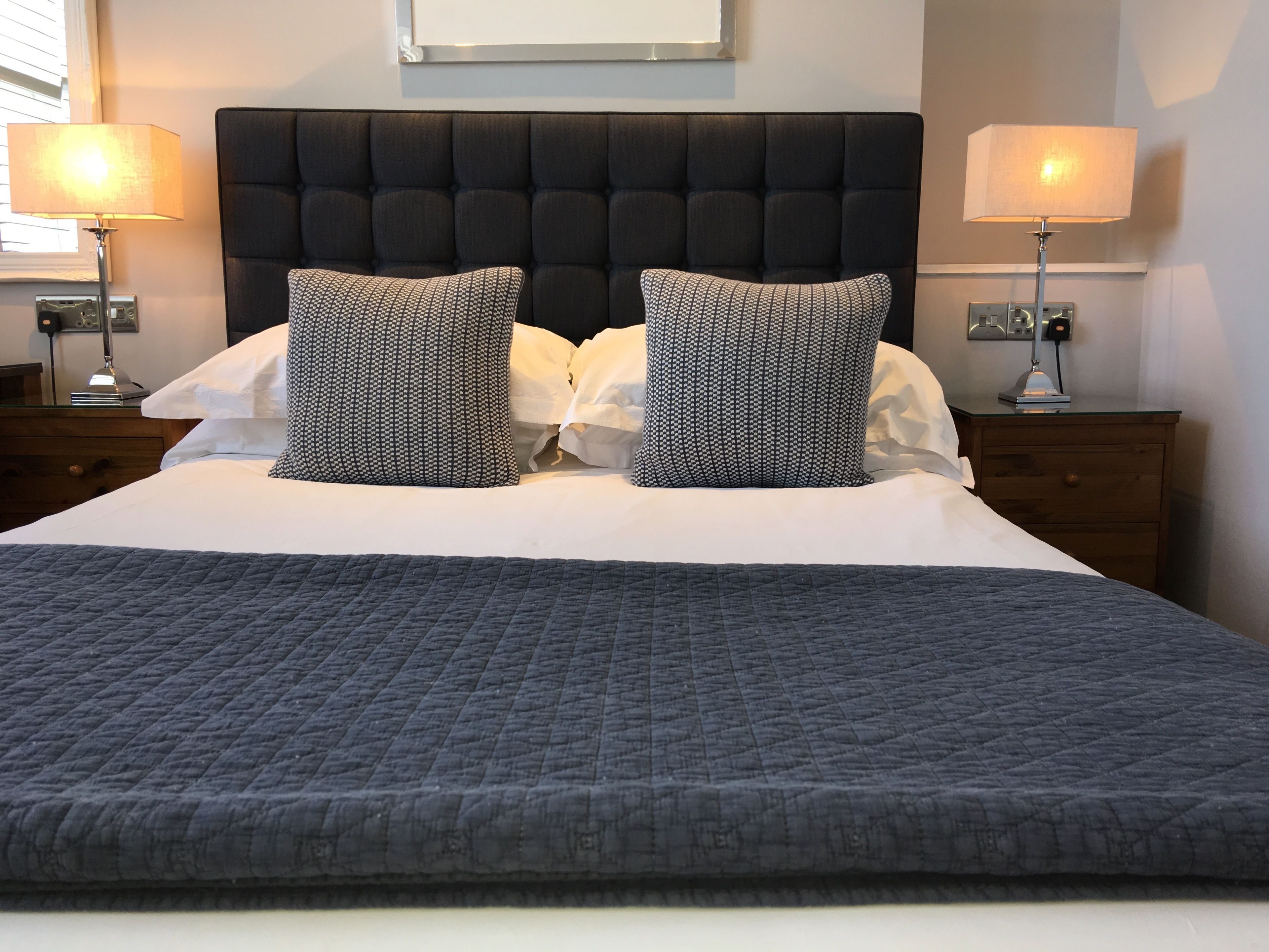 A neatly made bed with a dark headboard, two patterned pillows, and a grey quilt.
