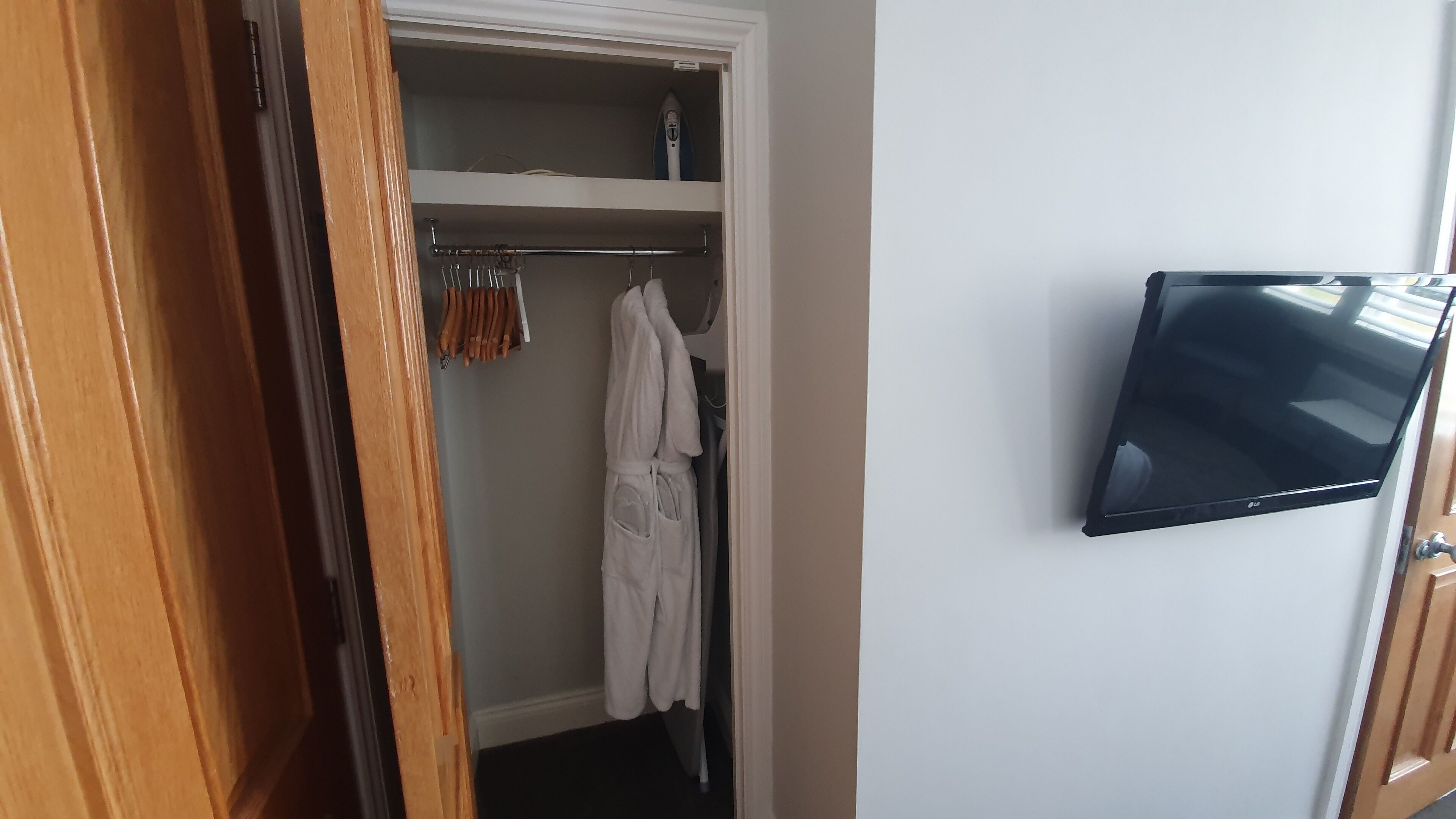 Une pièce avec une porte en bois, une robe blanche suspendue à un porte-manteau et un téléviseur à écran plat fixé au mur.
