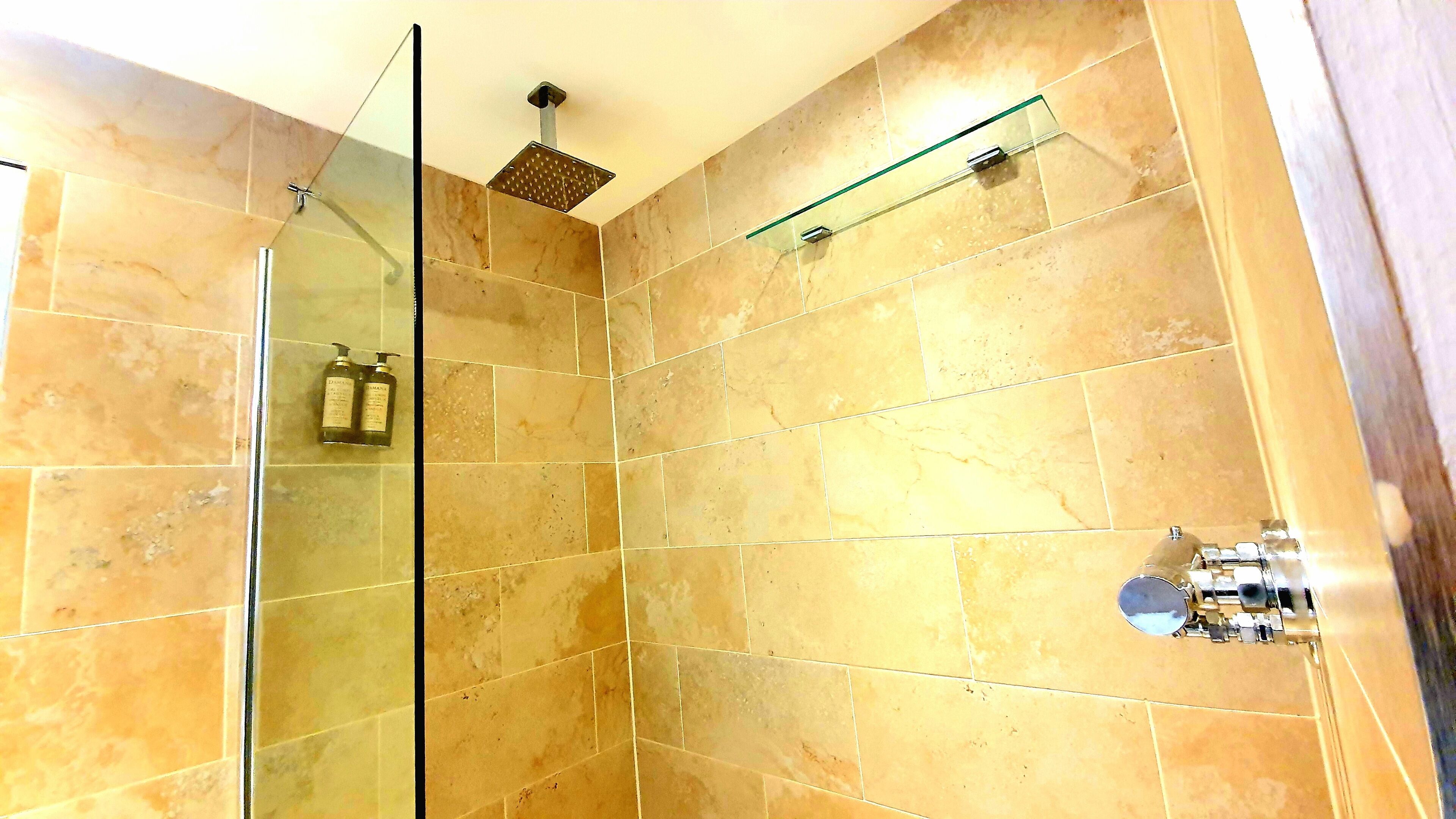 Ducha con puertas de vidrio, repisa de vidrio y cabezal de ducha manual.