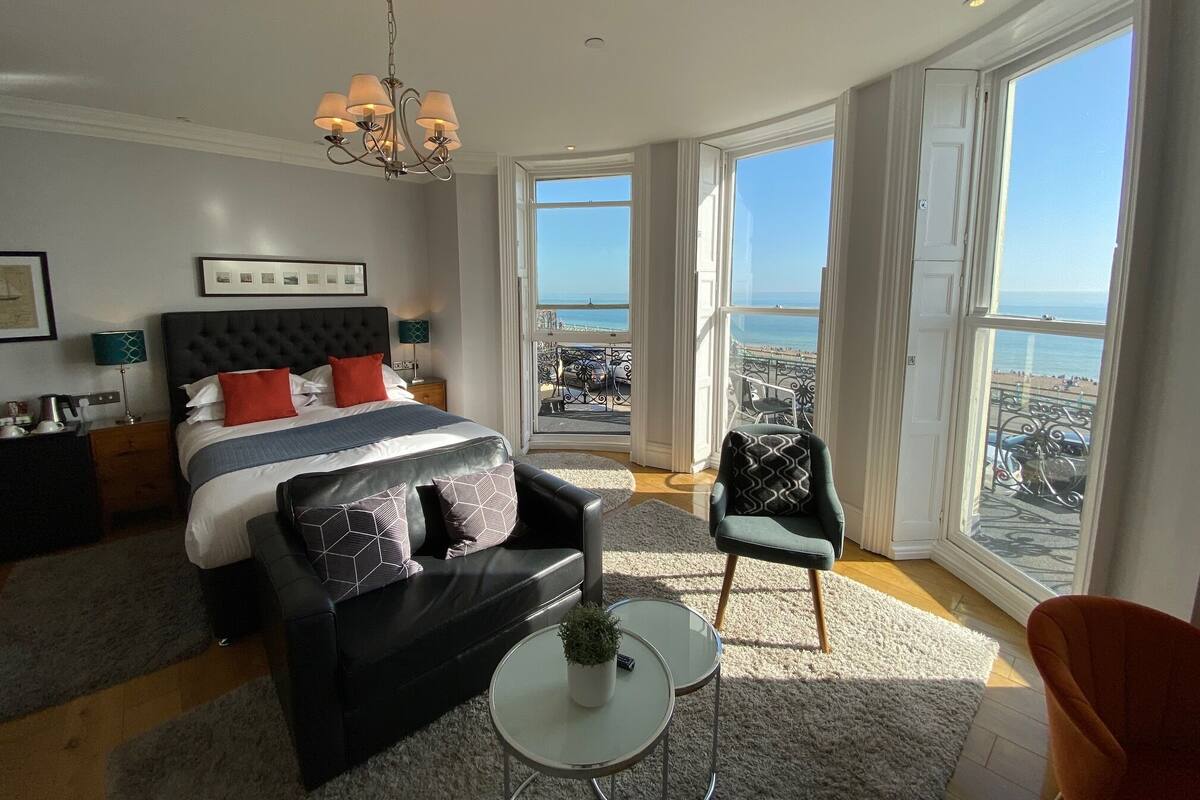 A modern bedroom with a large bed, a chandelier, a view of the sea, and a balcony.