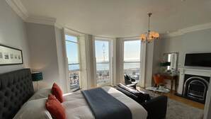 Un dormitorio con una cama grande, chimenea, televisor y balcón con vista al mar.