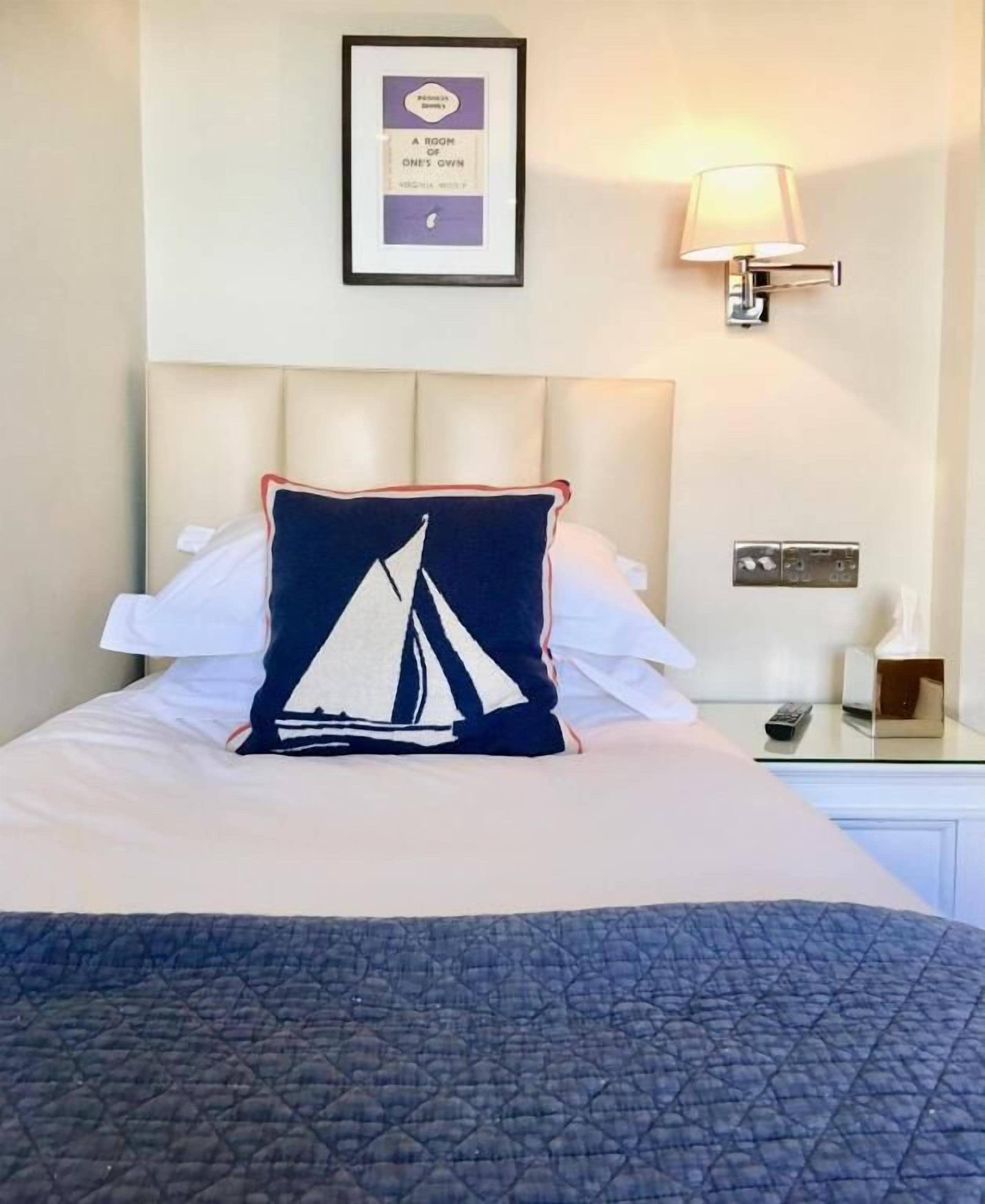 Een net opgemaakt bed met een kielkussen, een ingelijst citaat aan de muur en een bedlampje.