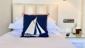 Een net opgemaakt bed met een kielkussen, een ingelijst citaat aan de muur en een bedlampje.