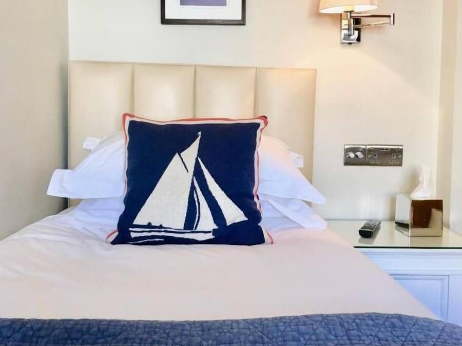 Een net opgemaakt bed met een kielkussen, een ingelijst citaat aan de muur en een bedlampje.