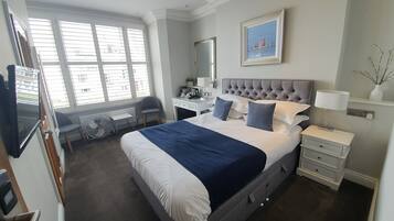 A hotel room with a large bed, a desk, a chair, a mirror, and a window with blinds.