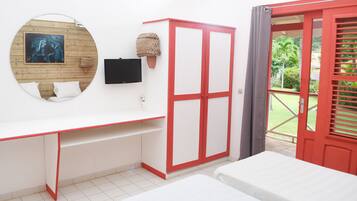 A room with a white desk, a red wardrobe, a bed, a TV, and a view of a garden.
