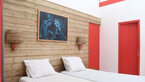 Une chambre avec deux lits, une tête de lit en bois, un tableau abstrait encadré et des portes rouges.
