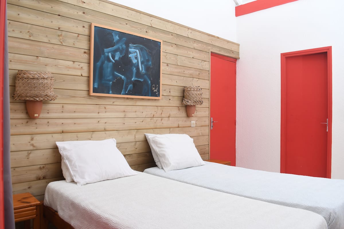 Een kamer met twee bedden, een houten hoofdbord, een lijst met abstract schilderij en rode deuren.