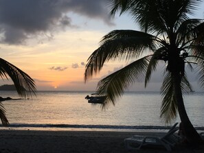 Escena de playa con palmeras, un bote y un atardecer.
