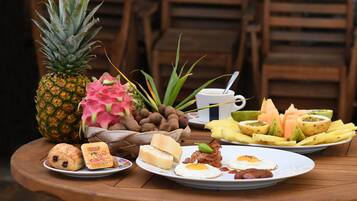Una mesa de desayuno con diversos alimentos, entre ellos una piña, pitahaya, pan, huevos y un plato de fruta.