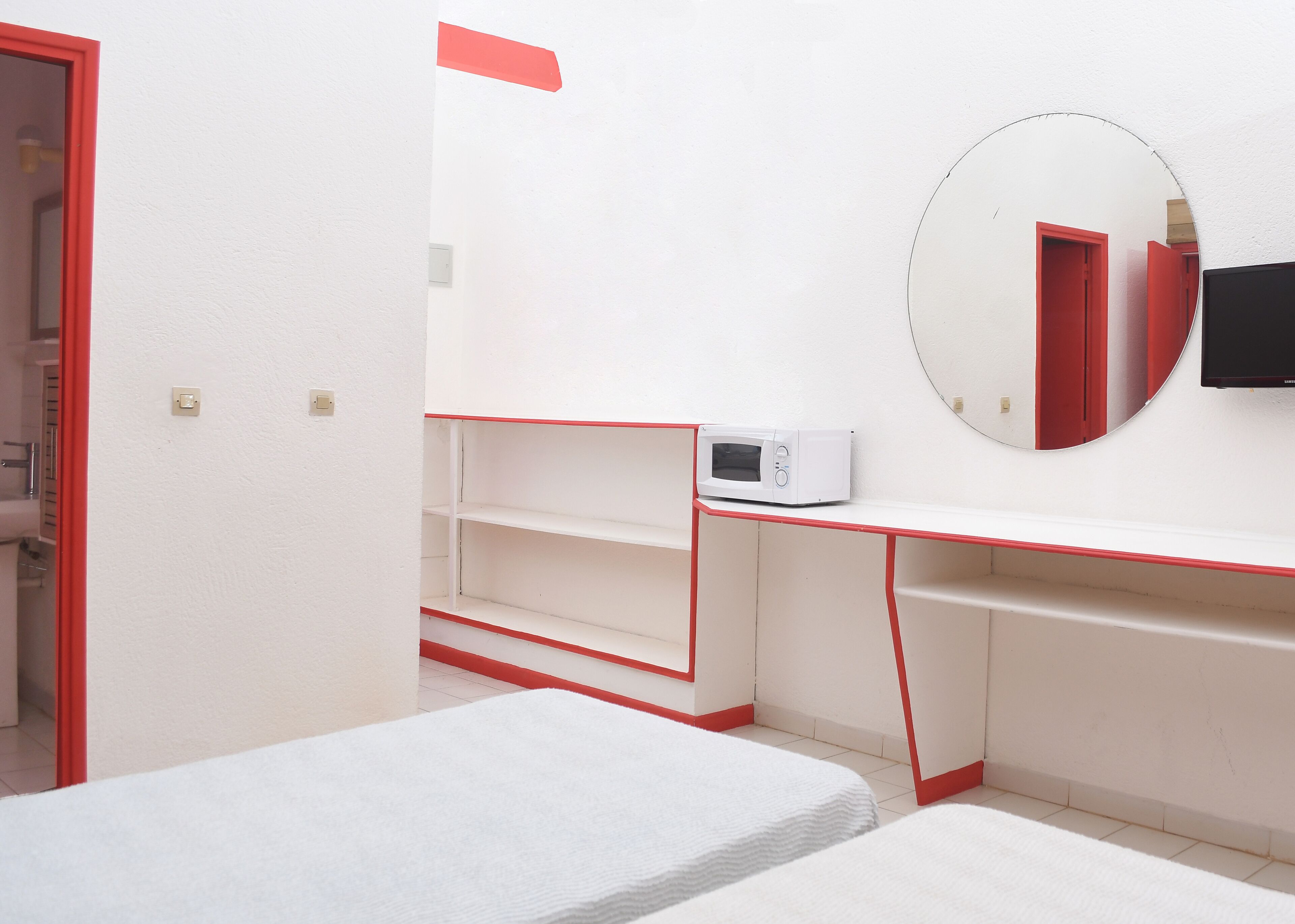 Una habitación pequeña con una cama, un escritorio con microondas y un espejo en la pared.