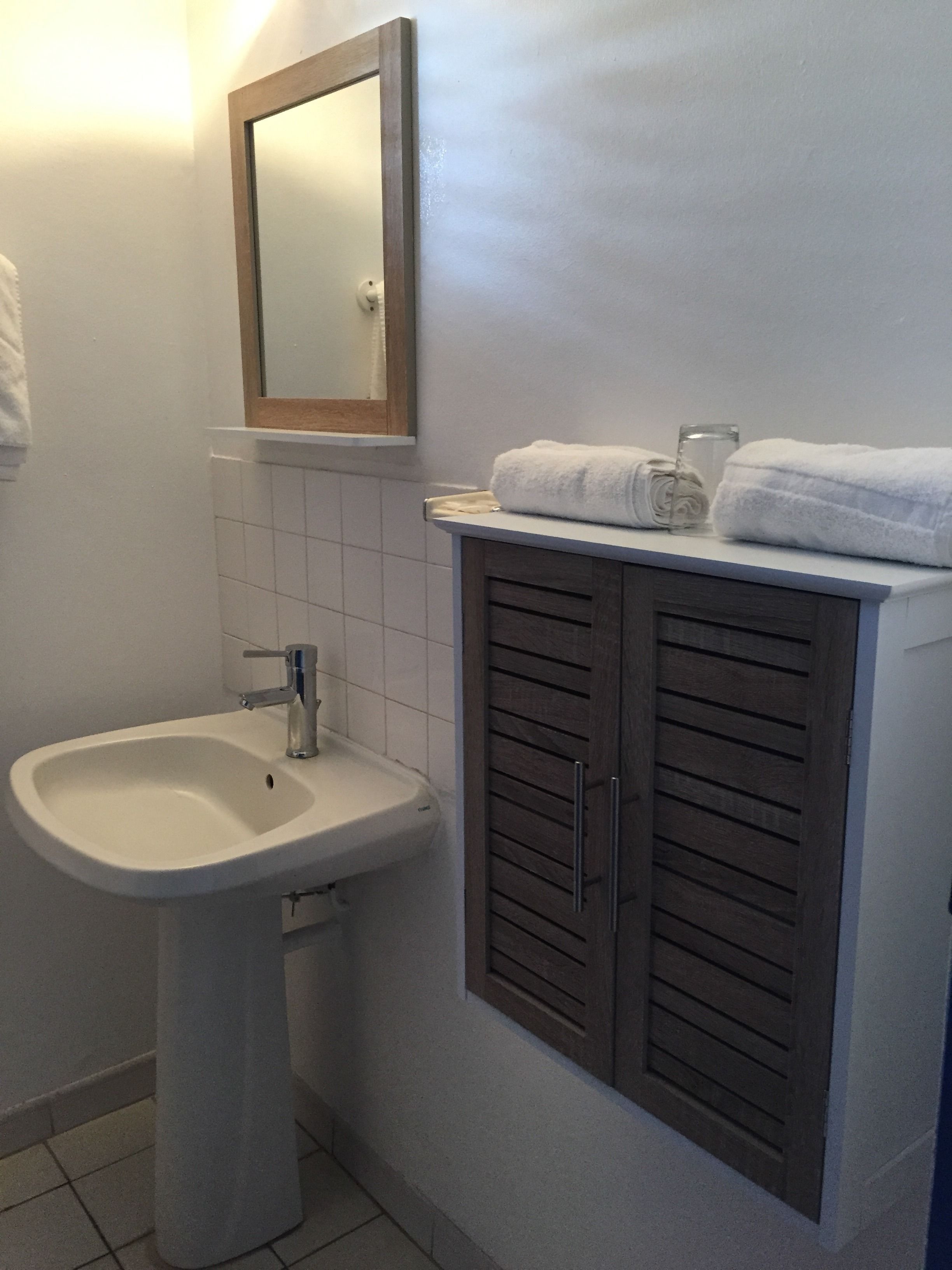 A bathroom with a white sink, a mirror, and a wooden cabinet with towels.