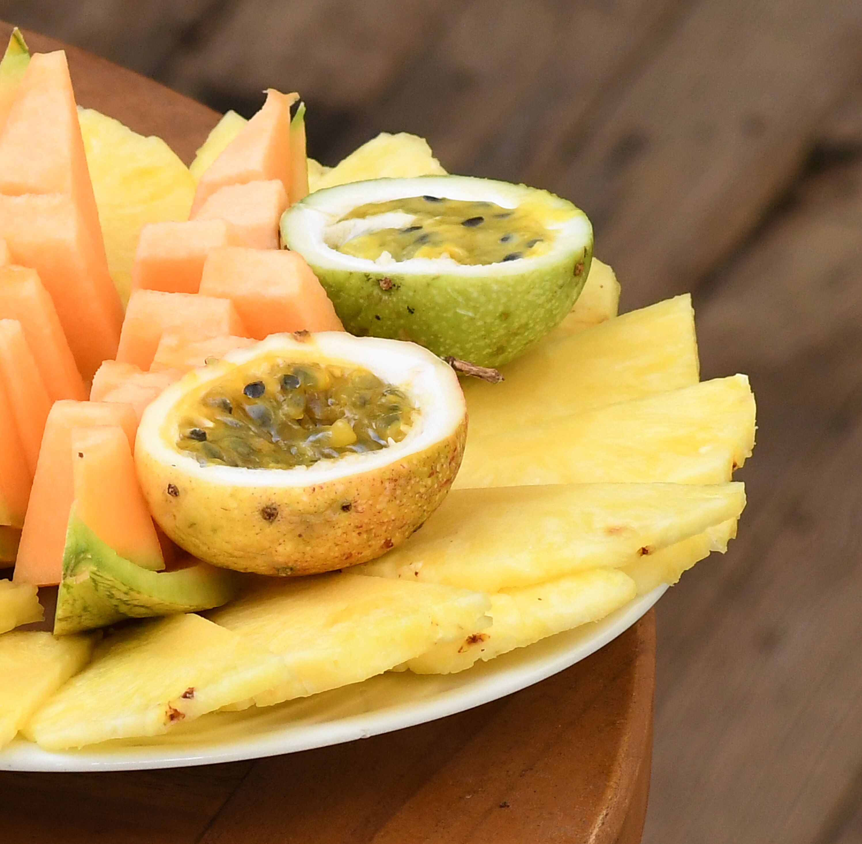 Une assiette de fruits coupés en tranches, notamment de l’ananas, du melon et de la fruit de la passion.