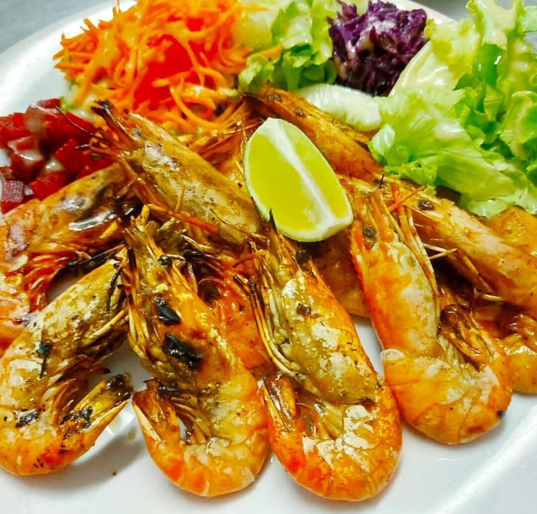 A plate of grilled shrimp with a wedge of lime and a side salad.