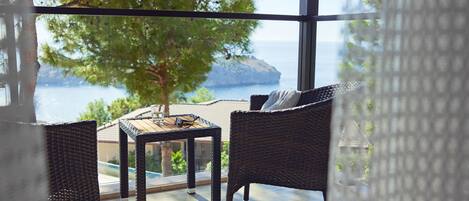 Uma varanda com móveis de vime, uma mesa e vista para o mar e uma árvore.