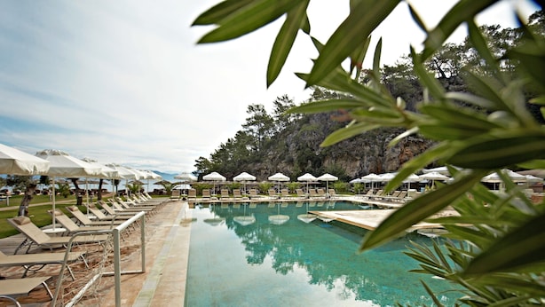 Una piscina con sillas de descanso y sombrillas, rodeada de vegetación y un paisaje pedregoso.