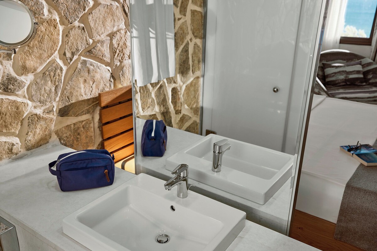 A bathroom with a stone wall, two sinks, a mirror, and a blue bag on the counter.