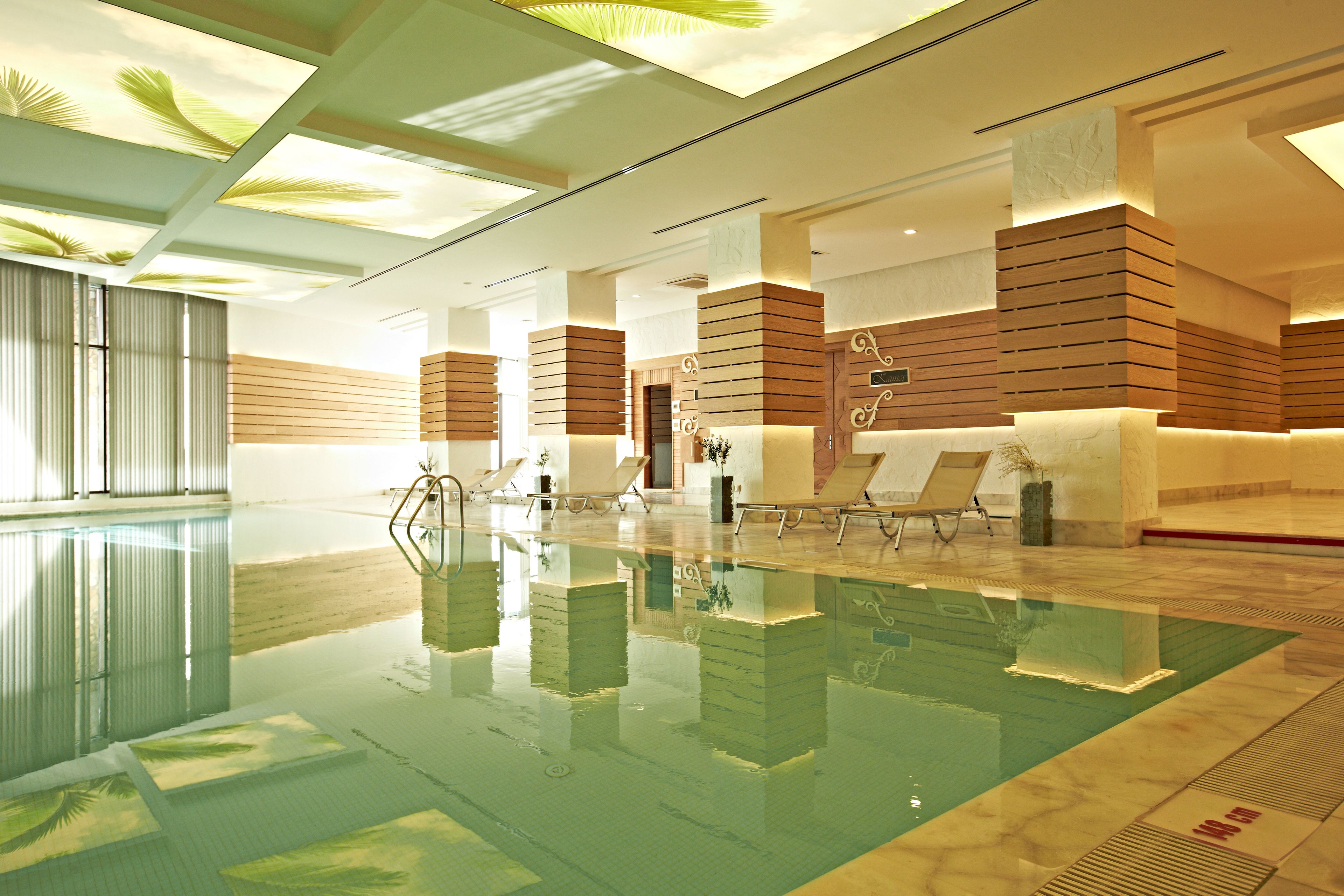A modern indoor swimming pool with clear water, wooden panel walls, and lounge chairs.