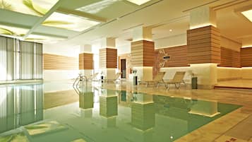A modern indoor swimming pool with clear water, wooden panel walls, and lounge chairs.