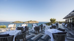 An outdoor dining area with tables and chairs, overlooking a body of water and a distant island.