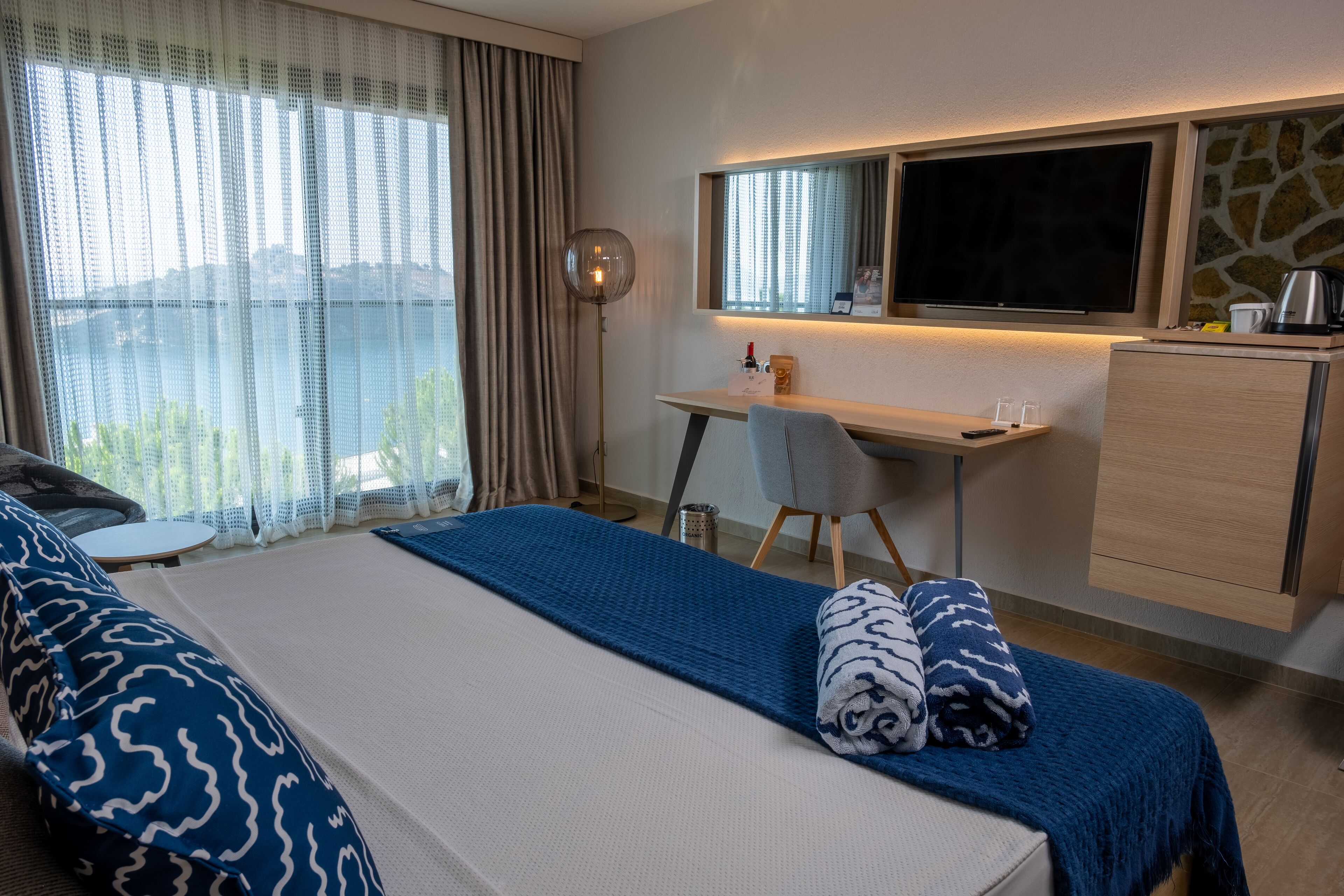 Ein Hotelzimmer mit Bett, Schreibtisch, Stuhl, Fernseher und Blick ins Freie.