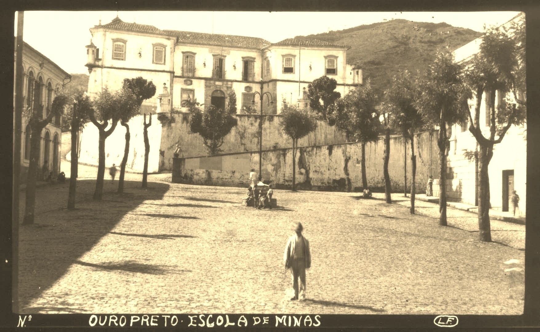 An old building with a courtyard, trees, and a person walking.