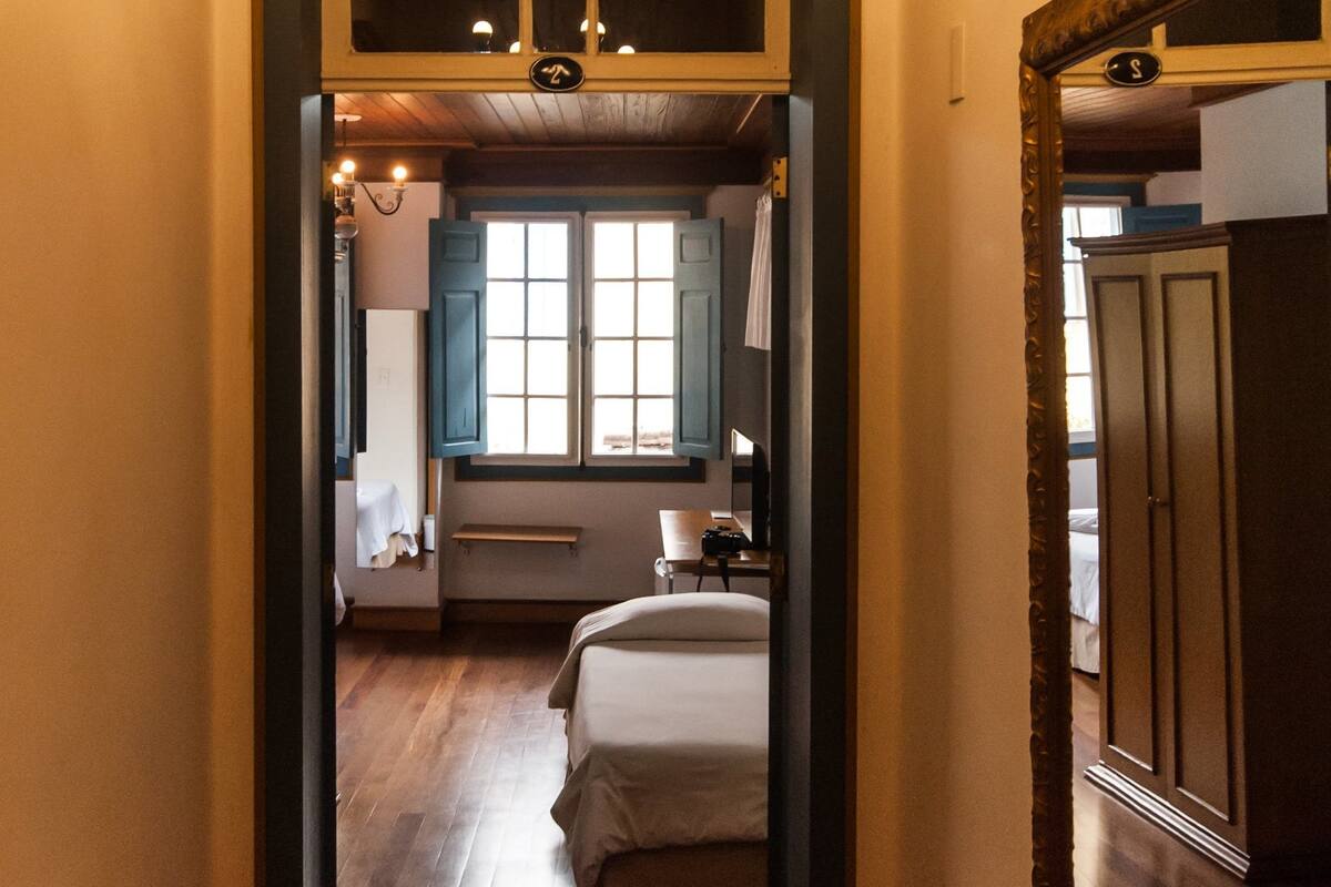 Een gang die leidt naar een slaapkamer met een houten vloer, een kroonluchter en een grote spiegel aan de muur.