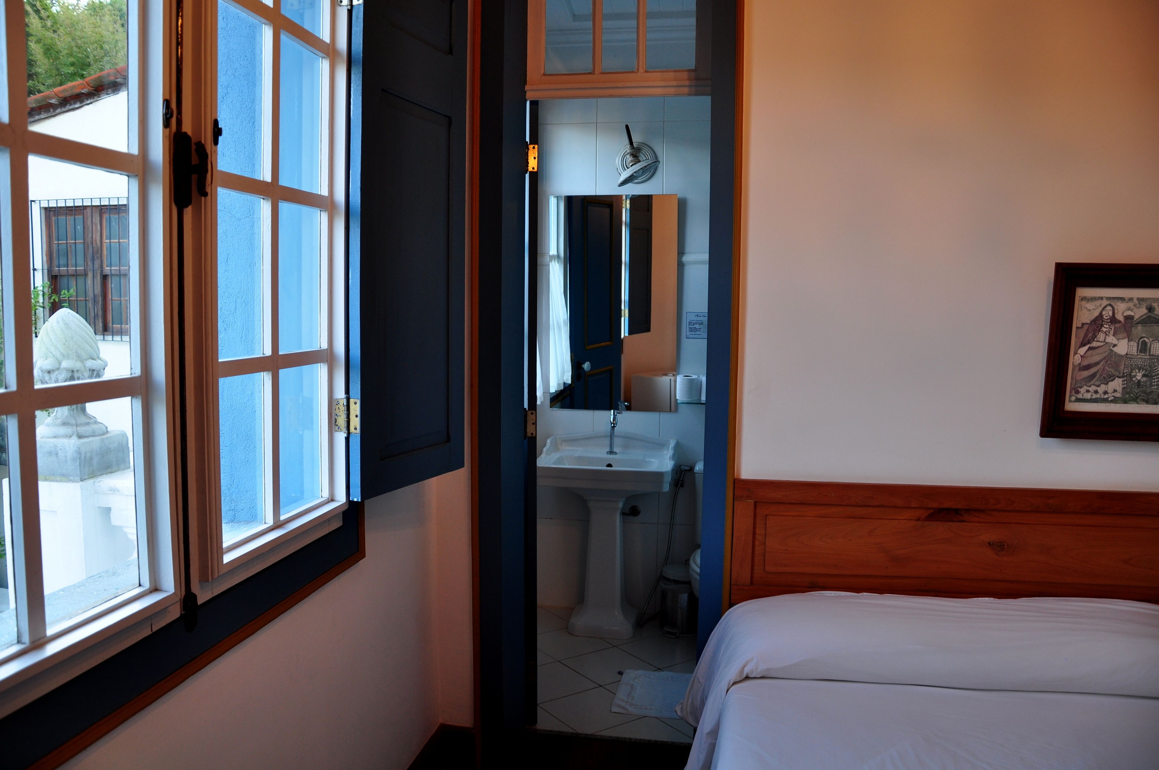 Una habitación con cama, ventana, lavabo y espejo.