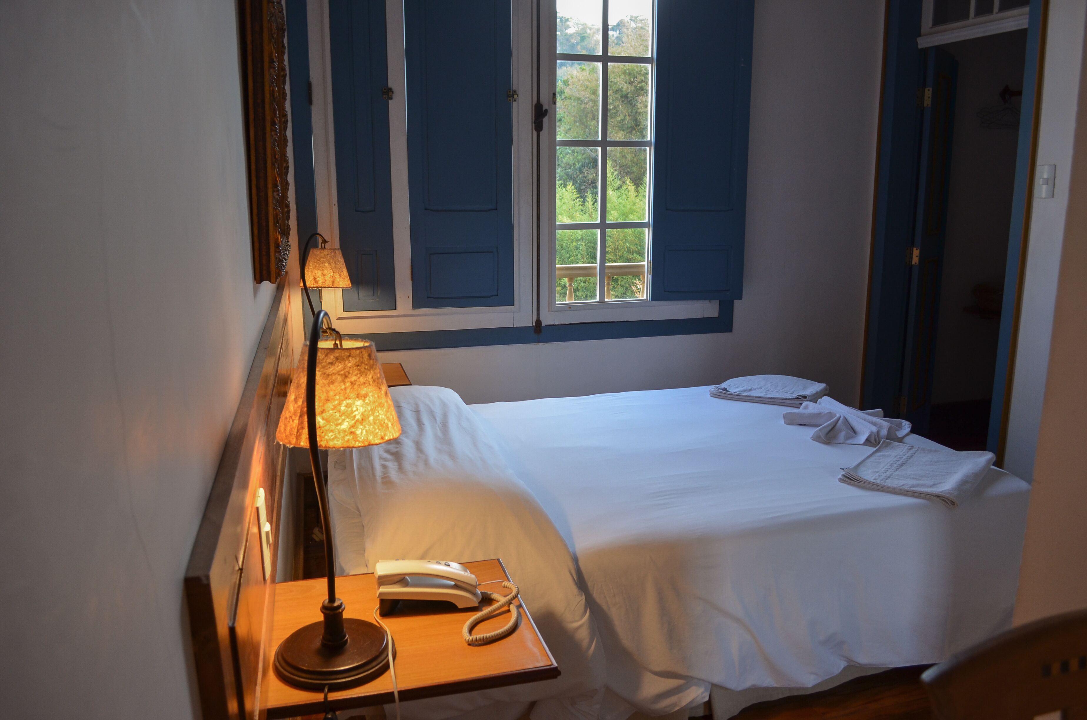 A neatly made bed with white linens, a bedside lamp, and a telephone on a wooden nightstand.