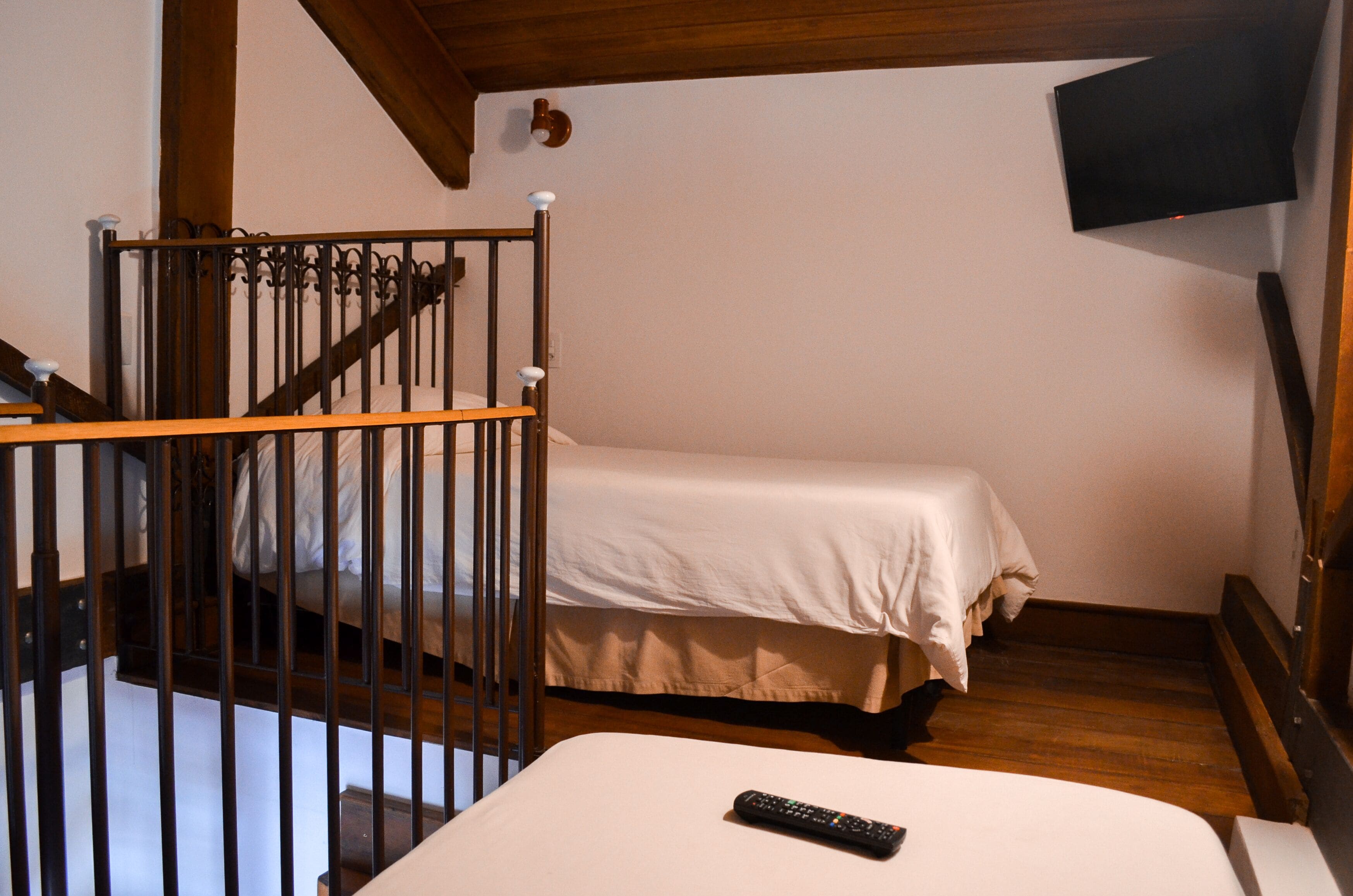 A bedroom with a bed, a wooden staircase, and a remote control on the bed.