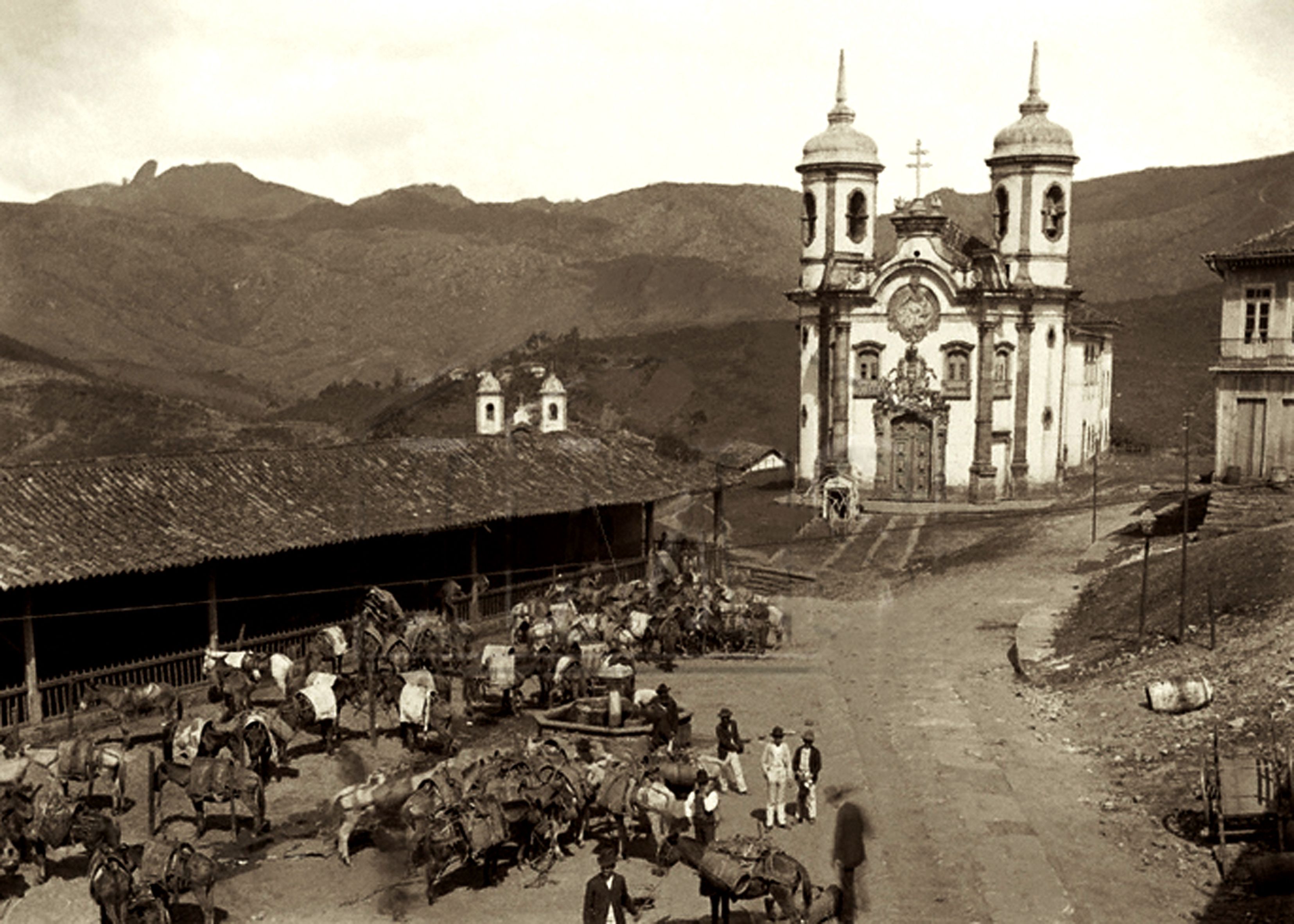 A historical scene with a church, a stable with horses, and a mountainous backdrop.