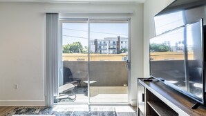 Una sala de estar moderna con un televisor de pantalla plana grande, un ventanal corredero que da a un balcón y un diseño minimalista.