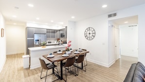Una cocina moderna con electrodomésticos de acero inoxidable, un comedor con mesa y sillas de madera, y un reloj de pared.