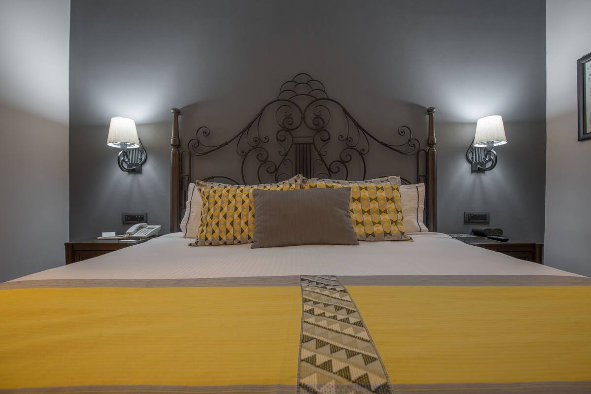A neatly made bed with patterned pillows, a decorative headboard, and wall-mounted lamps on either side.