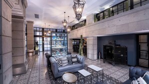 A lobby with a grey sofa, a coffee table, and a fireplace. There is a glass display case with various items and a large window in the background.