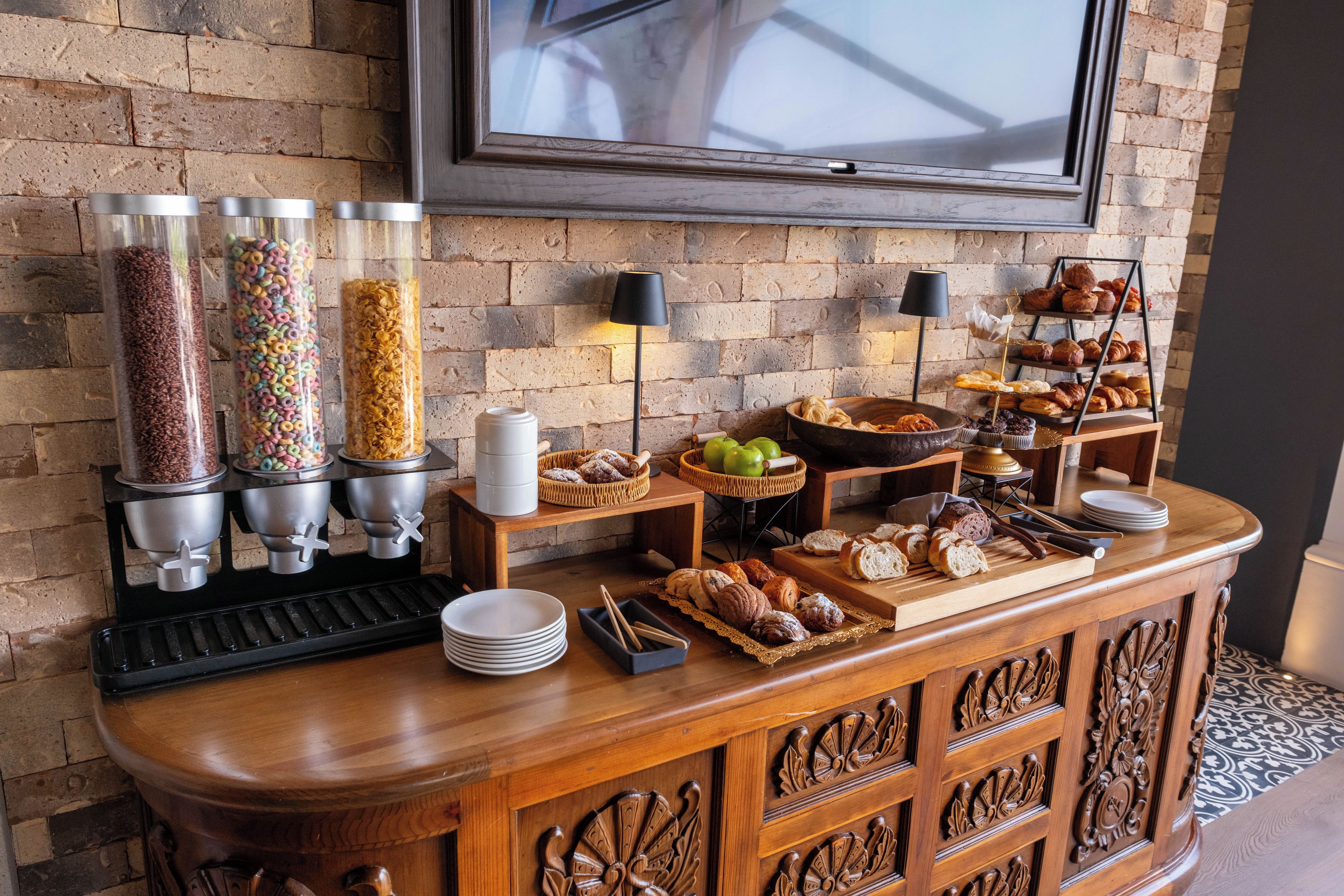Un bufé de desayuno con diversas opciones de comida, una máquina de café y un televisor montado en la pared.