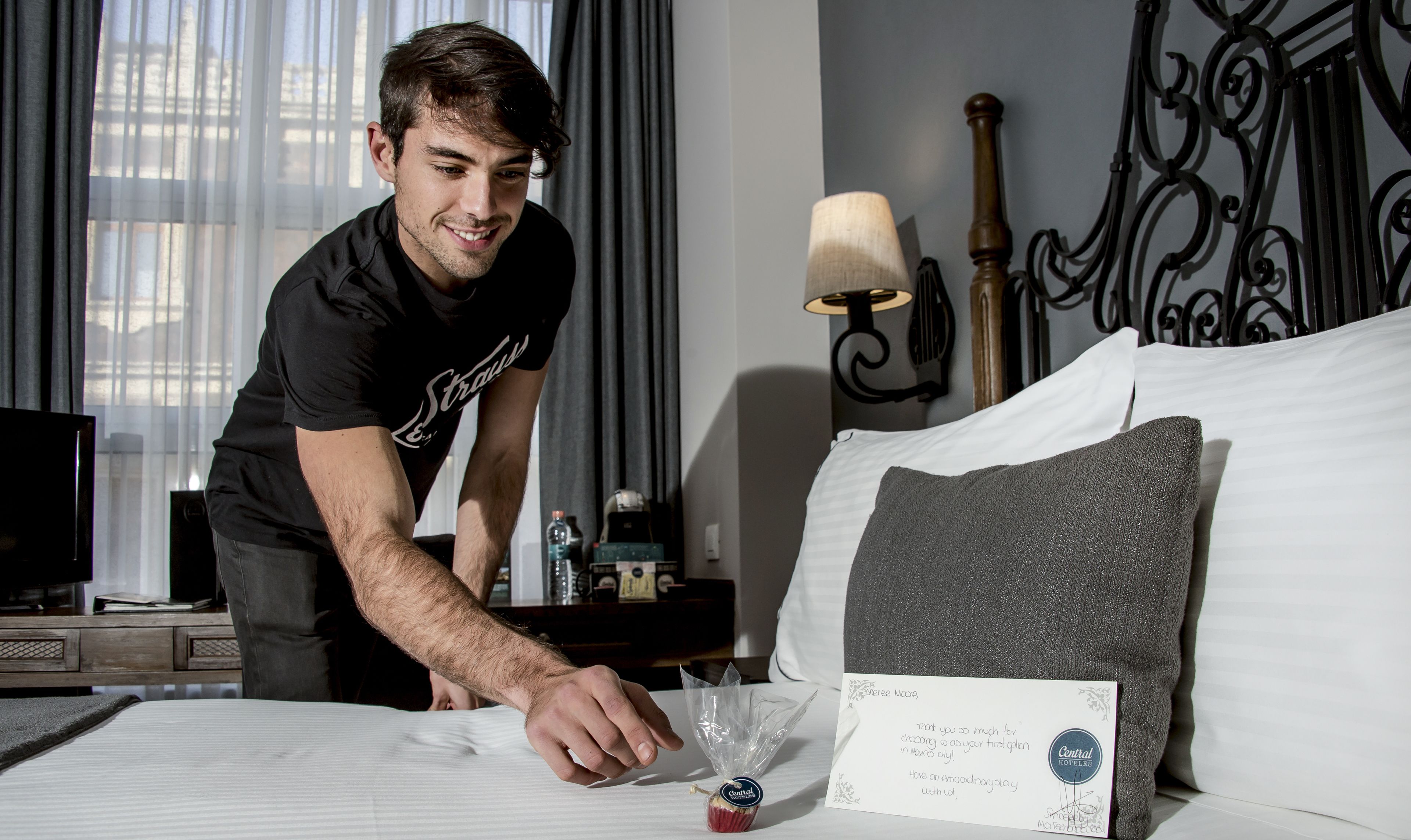 A hotel room with a neatly made bed, a bedside table with a lamp, and a decorative wall piece.