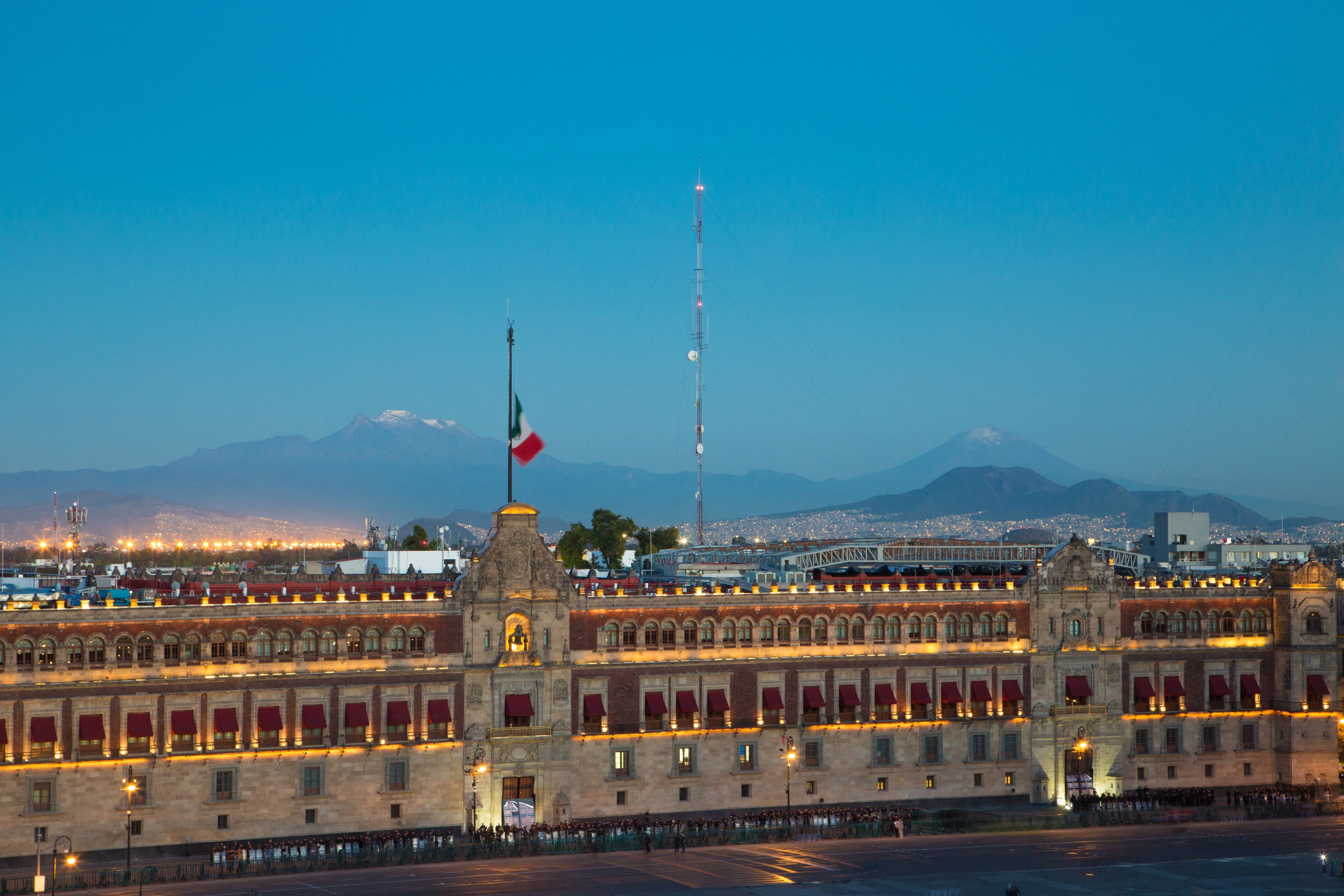 A historic building with a prominent tower and a flag, featuring a large open plaza in front.