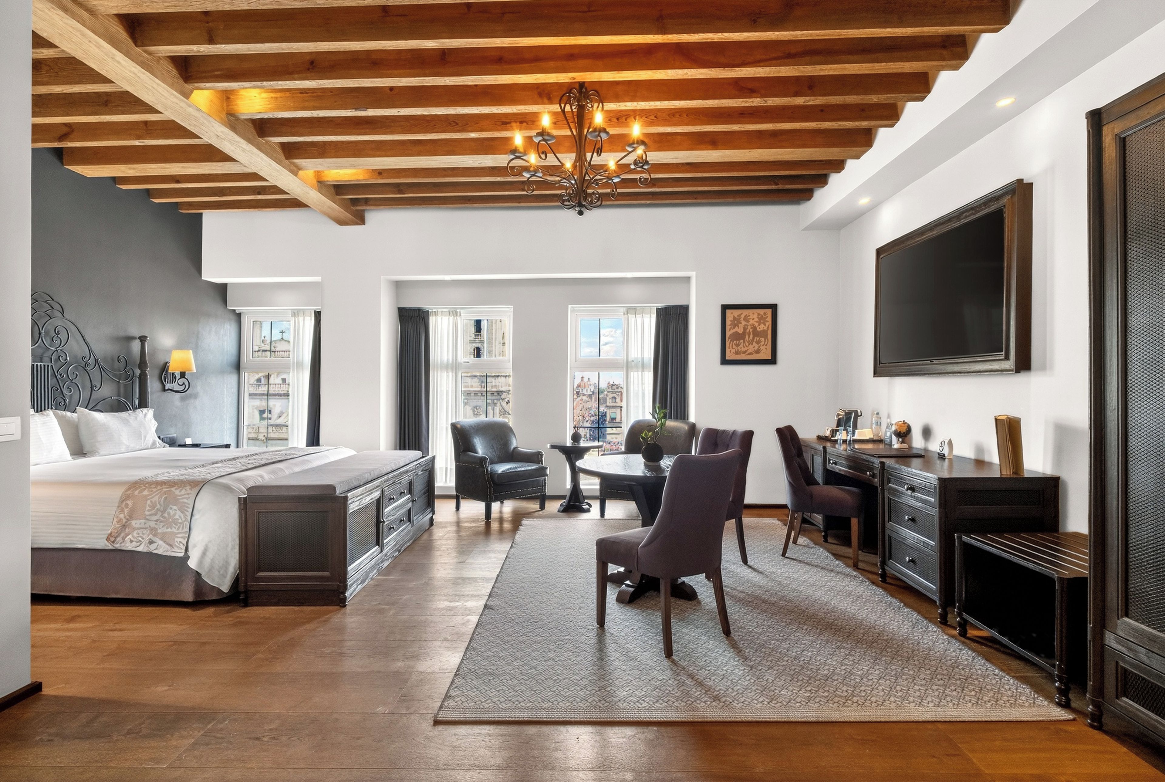 Une chambre d’hôtel avec un lit, un bureau, une chaise, une télévision et un lustre.