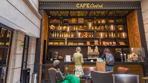 A café with a green wall and hanging lights, seating areas, and a bar counter.