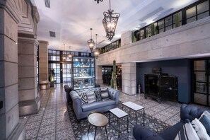 A spacious lobby with a high ceiling, a seating area with a sofa and armchairs, a glass display case with decorative items, and a large window with a view of the sky. - Hotel Zócalo Central (Mexico City)