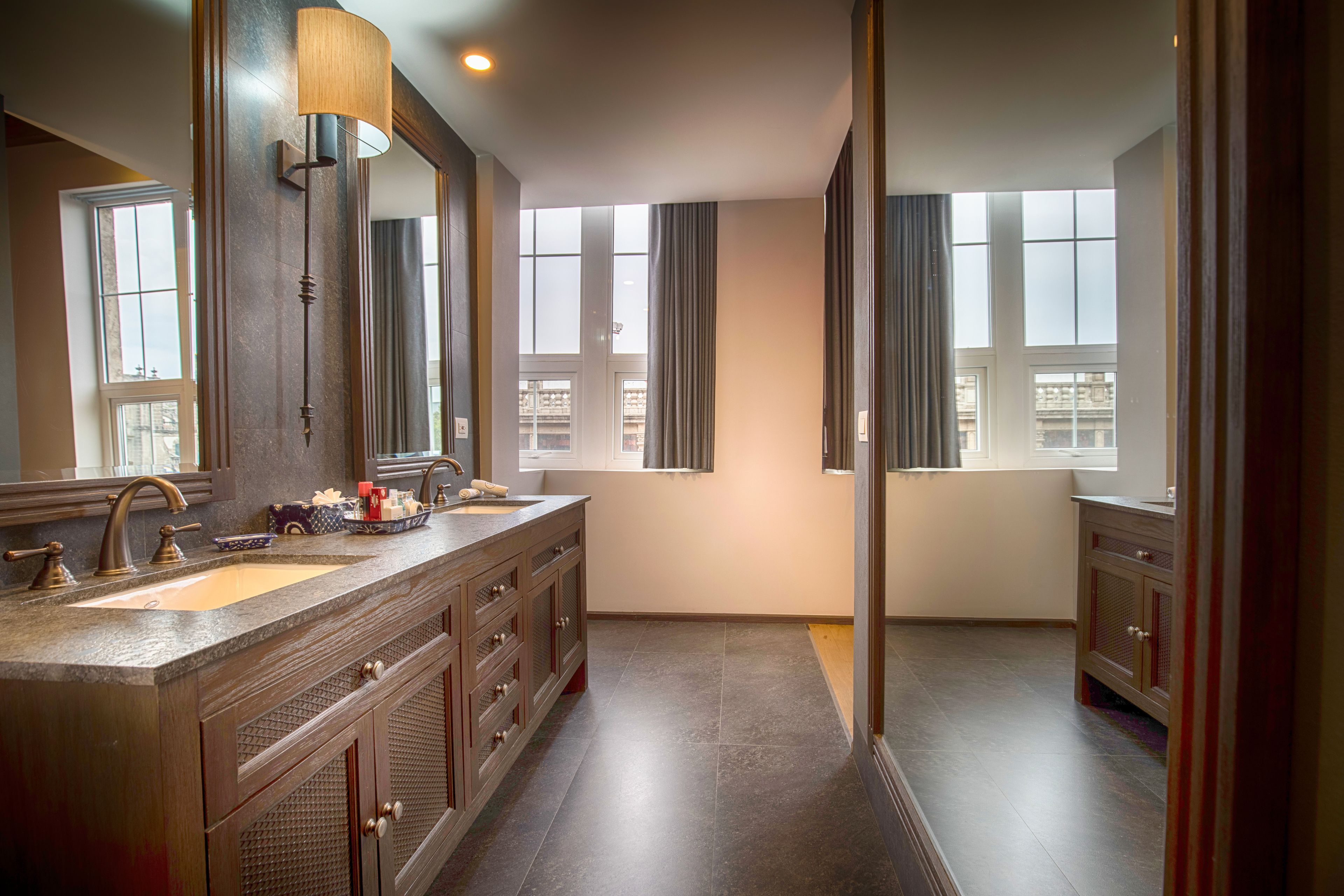 A modern bathroom with a double sink vanity, large mirrors, and a view of the city through large windows.
