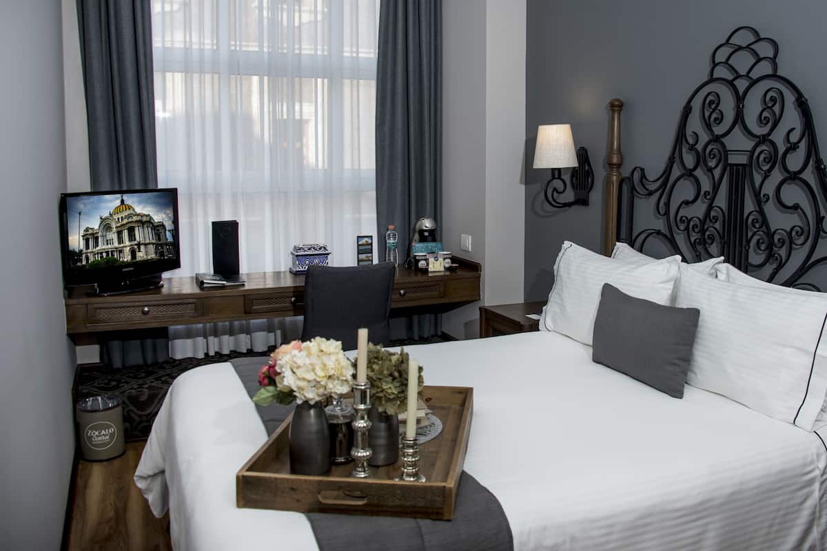 A hotel room with a large bed, a desk with a television, a lamp, and a decorative headboard.