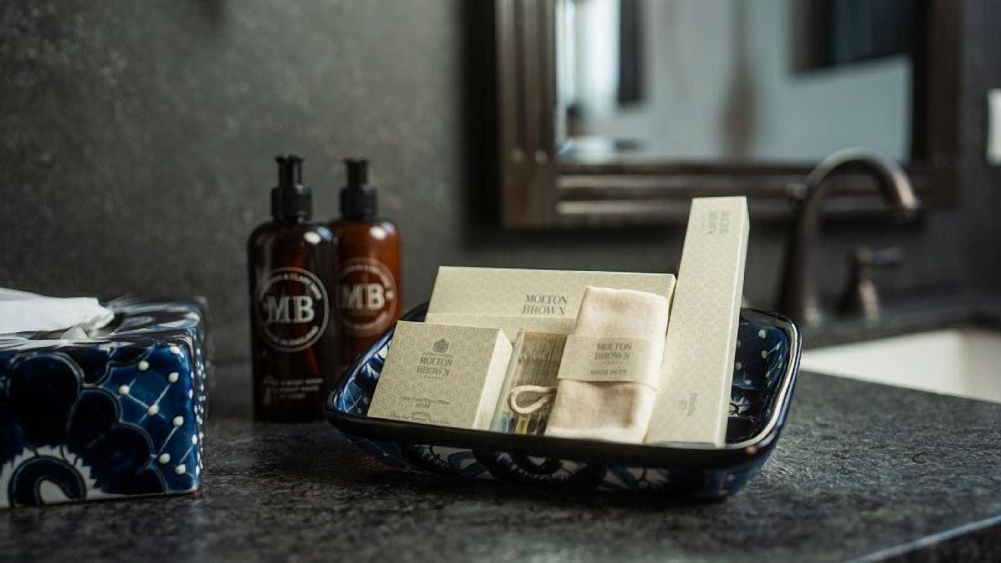 Un ripiano del bagno con articoli da toilette, tra cui una tazza blu, due flaconi di sapone Molton Brown e un vassoio con una saponetta e una barra di lozione.